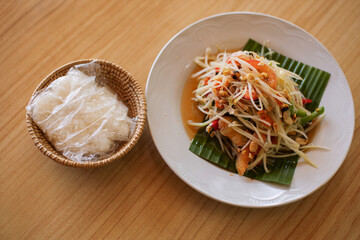 Thai food papaya salad with sticky rice placed on a white plate ready to eat.