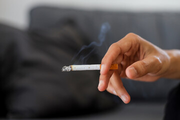 Man's hand holding a cigarette near a sofa at home