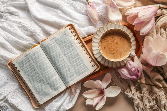 Open Bible on a cozy white and beige fabric with a cup of coffee and magnolia flowers around, symbolizing peaceful morning devotion or spiritual spring atmosphere