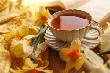 A close-up of a cup of tea with yellow daffodils and stacked books, creating a warm and cozy...