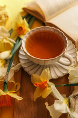 A close-up of a cup of tea with yellow daffodils and stacked books, creating a warm and cozy springtime setting with natural light and soft tones