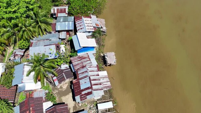 Tilt-up aerial shot reveals shanty homes and squat dwellings lining the Agusan River banks in Butuan, Mindanao, Philippines.