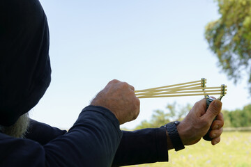 Hooded man aiming with a powerful slingshot in a field
