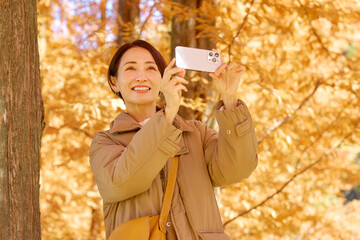 紅葉の動画をスマホで撮影する女性　ミドルエイジ