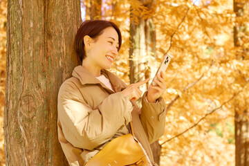 紅葉の中でスマホを使う女性　ミドルエイジ