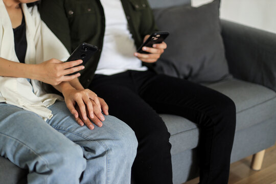 Couple sitting on couch with their phones while holding hands
