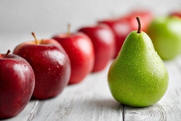 One green pear standing out among red apples on white wood.