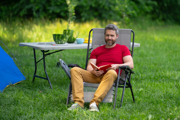 Fototapeta premium Man enjoying camping in nature. Summer trip on nature. Tourist relaxing in forest camp. Camping trip. Resting near tent after hiking. Freedom vacation in a peaceful campsite. Man on Picnic in summer.