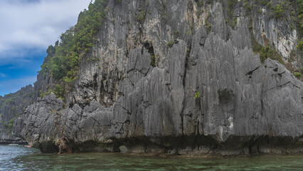 Picturesque cliffs surround the emerald lagoon. There is green tropical vegetation on the steep,...