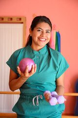 Physiotherapist smiling and holding weights and pilates ball in rehab center