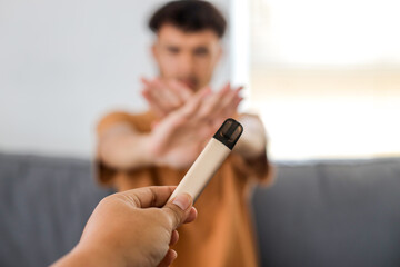 Teenager boy shows a sign of rejection of disposable e-cigarette with hand