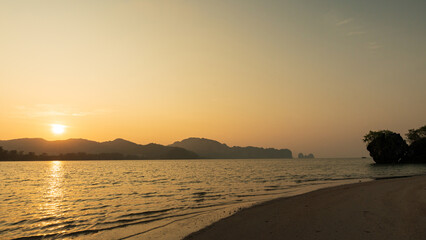 Fototapeta premium Golden sunset over a quiet beach with calm sea and distant mountain silhouettes.