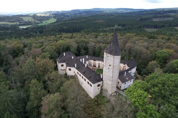 Fototapeta premium Aerial view of medieval Rostejn Castle with defensive tower on forested hill, Czech heritage site.