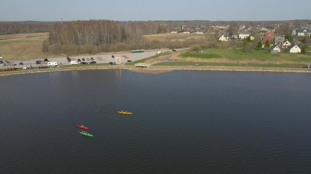 Aerial droen footage slowly following 3 kayaks boats who are rowing and paddling on a calm murky muddy brown colored water during a sunny day in southern Estonia Tamula lake. green shoreline visible.