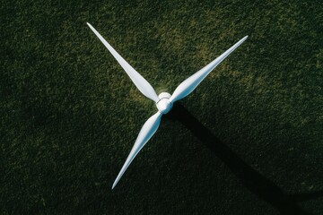 Overhead view of a wind turbine's blades atop a grassy field  The blades are white and extend from a central hub, casting a shadow on the ground