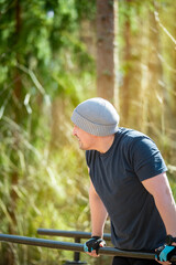 Man performing bodyweight dips on parallel bars in a forest fitness park. Wearing gloves and a...