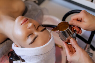 A woman is receiving a Japanese head spa treatment at a beauty salon. The therapist gently pours water, liquid onto her forehead to enhance relaxation of a scalp. Atmosphere promotes stress relief