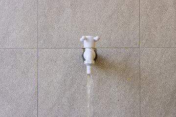 White faucet on tiled wall with water flowing down. Minimalist plumbing photo perfect for water supply, bathroom, or utility usage concepts in editorial or commercial use.