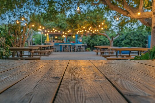 Wooden picnic tables under string lights in an outdoor restaurant setting Blurred background of tables, chairs, and a bar area  Wooden surface in foreground