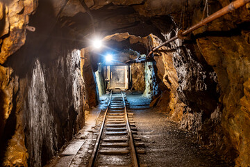 Naklejka premium This mine shaft in Jachymov, Czechia showcases the rich mining history of the area. Dimly lit tunnels lead into the depths, revealing tracks used for transporting minerals.