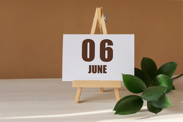 June 6th. Day 6 of month, Calendar date. Green branch, easel with the date and month on desktop. Close-up, brown background. Summer month, day of year concept