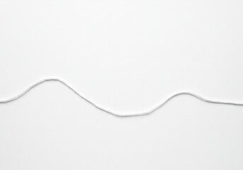 A single strand of gray thread or string laid in a wavy line on a plain white background surface view