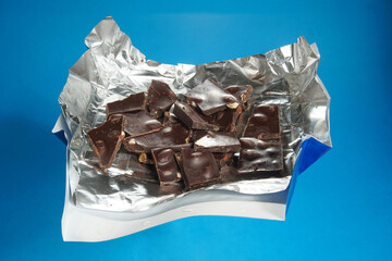Sweet and delicious broken chocolate bar with nuts on silver foil on a blue background.