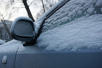 Rear view mirror and door window under snow and ice close up. The vehicle is covered with snow and...