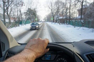 View from the cockpit of a car driving along a narrow snowy road with an oncoming car.