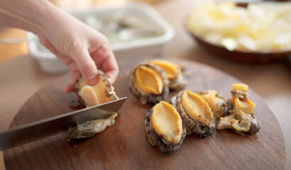Close-up of a hand slicing fresh abalone on a wooden cutting board, ideal for seafood preparation...
