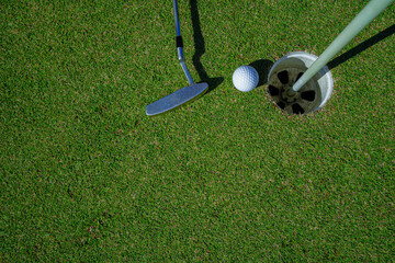 Obraz premium Top view of a golf ball with putter on green course at hole.