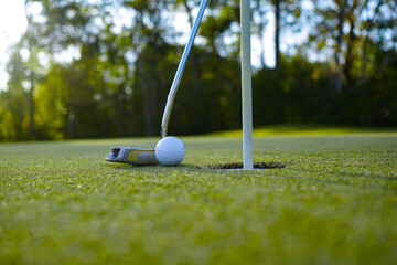 Top view of a golf ball with putter on green course at hole.