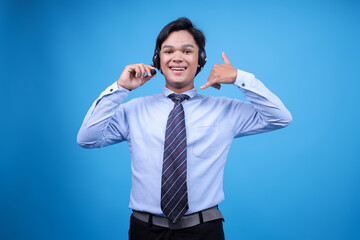 Portrait of young asian male customer service in headset making call gesture isolated on blue background.