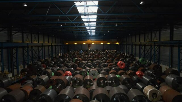 Drone slowly flying through a dark warehouse filled with large steel coils