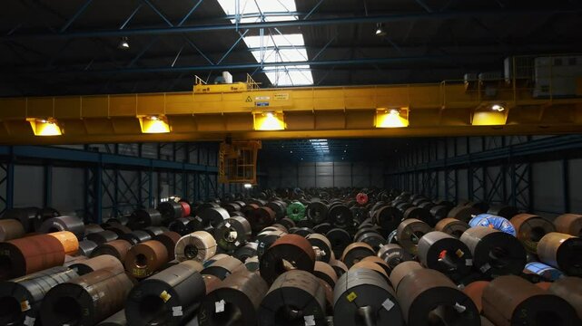 Stunning view of a large overhead bridge crane moving through a dark warehouse filled with heavy steel coils