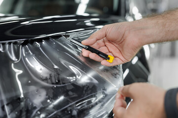 Worker is applying transparent film to a car to protect it from gravel and scratches on the hood of a car.