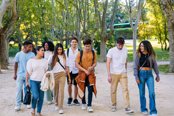 Group of diverse cheerful university students walking together in a park, talking and having fun