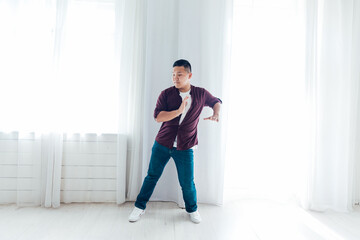 Asian man dancing to music alone in white room