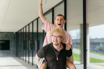 Two cheerful young men celebrate outdoors with a playful piggyback ride and joyful laughter,...