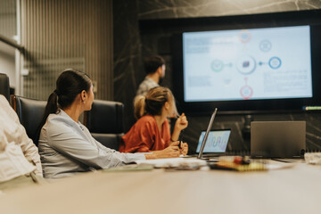 A group of business people attentively listen during a late-night presentation in the office. They...