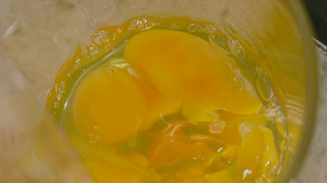 Overhead View of Raw Eggs Being Poured in Slow Motion into Measuring Jug with Multiple Eggs Ready to Make Scrambled Eggs for High Protein Breakfast.