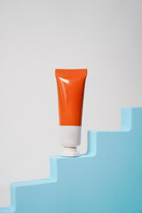 orange and white skincare tube packaging with blue staircase decoration podium on white background