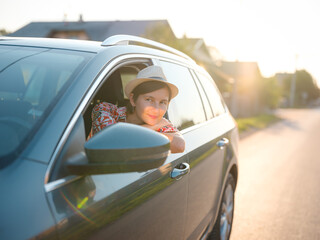 Naklejka premium Traveler woman in red ethnic dress and hat drives car through scenic countryside of Croatia in summer. Surrounded by lush fields and forests, she enjoys peaceful and adventurous road trip