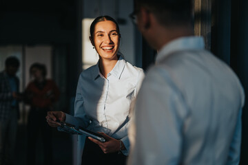 A diverse group of business people engaging in a friendly conversation in an office hallway. The...