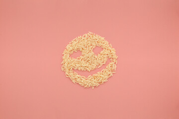 Creative food concept photo of smiley face made of rice on pink background.