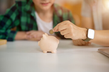 A father is teaching his son how to save money by putting money in a piggy bank.