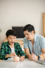 A father is teaching his son how to save money by putting money in a piggy bank.