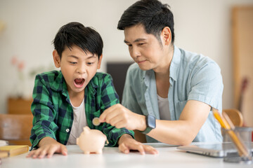 Fototapeta premium A father is teaching his son how to save money by putting money in a piggy bank.