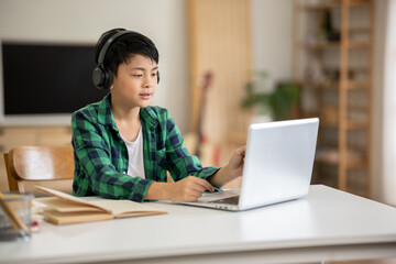 A boy is studying online intently on his laptop at home.
