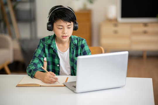 A boy is studying online intently on his laptop at home.